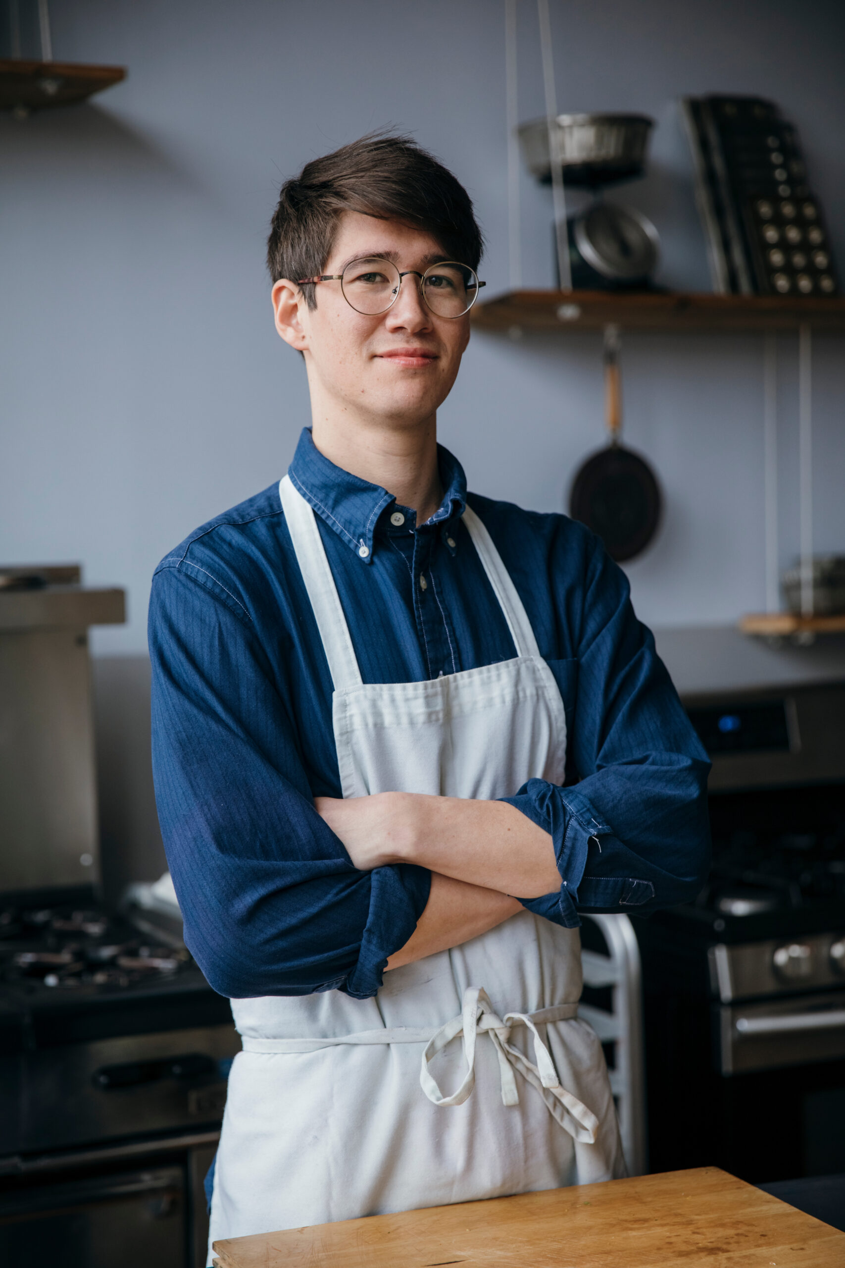 Portrait of smiling male chef with arms crossed wearing eyeglasses while standing by table against wall in training class