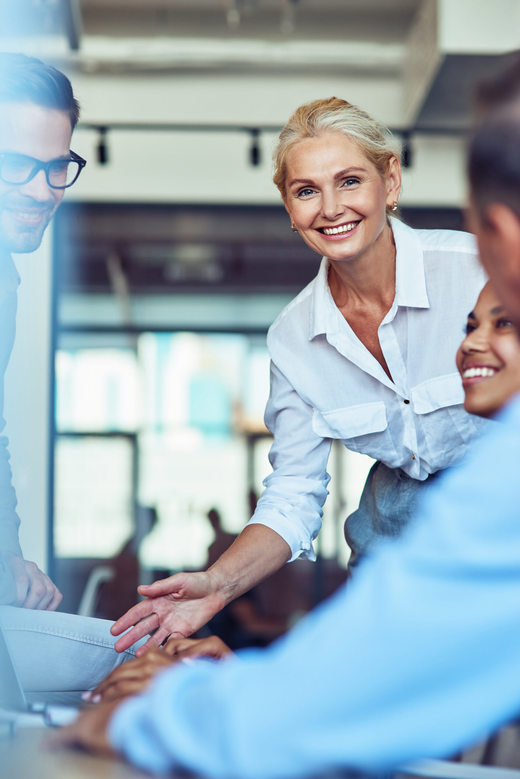 Young cheerful mature businesswoman smiling at camera while having a meeting with multiracial colleagues at office. Teamwork and collaboration concept